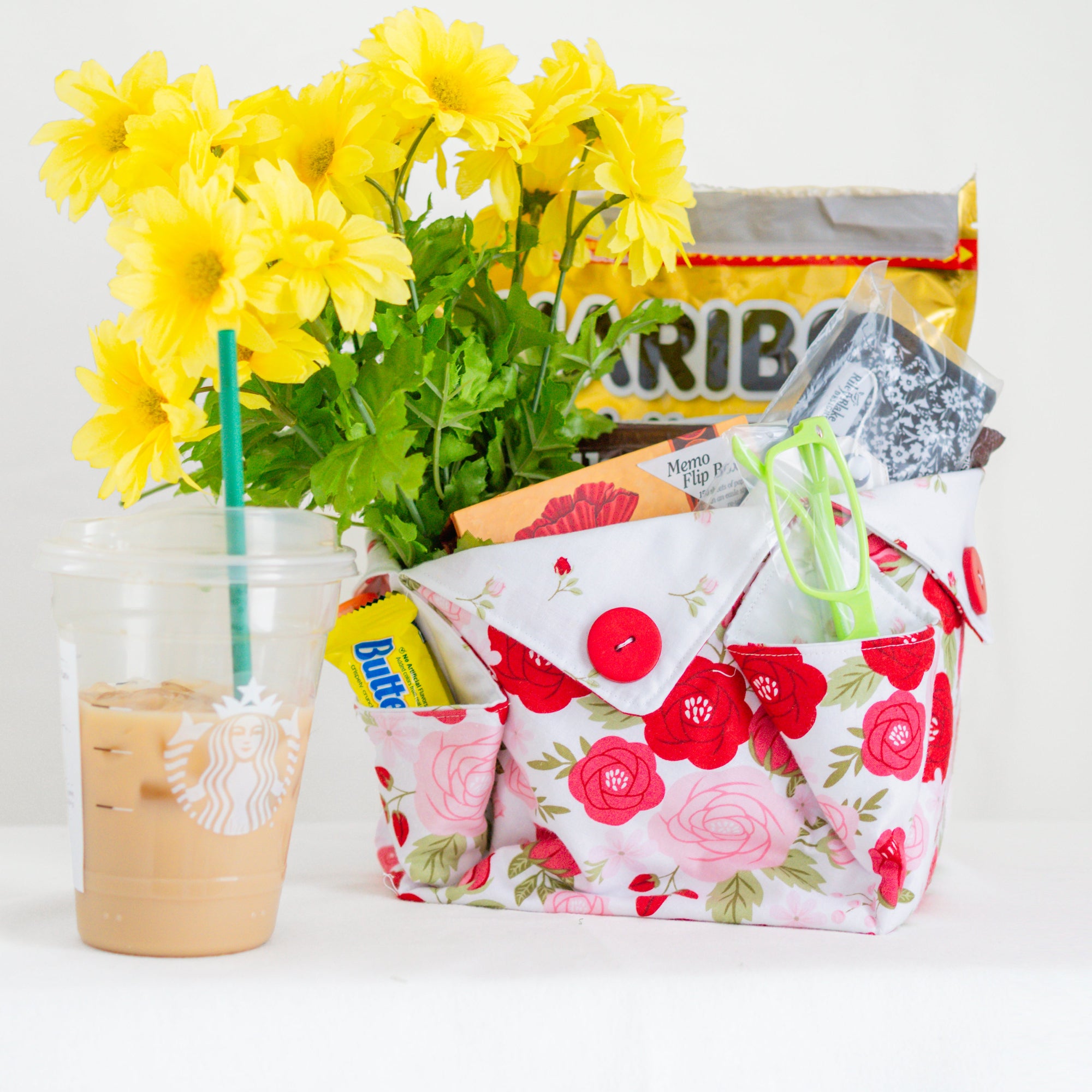 Floral-patterned bag with snacks and a glass of iced coffee on a white background