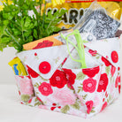 Floral-patterned fabric basket with snacks and a plant on a white surface