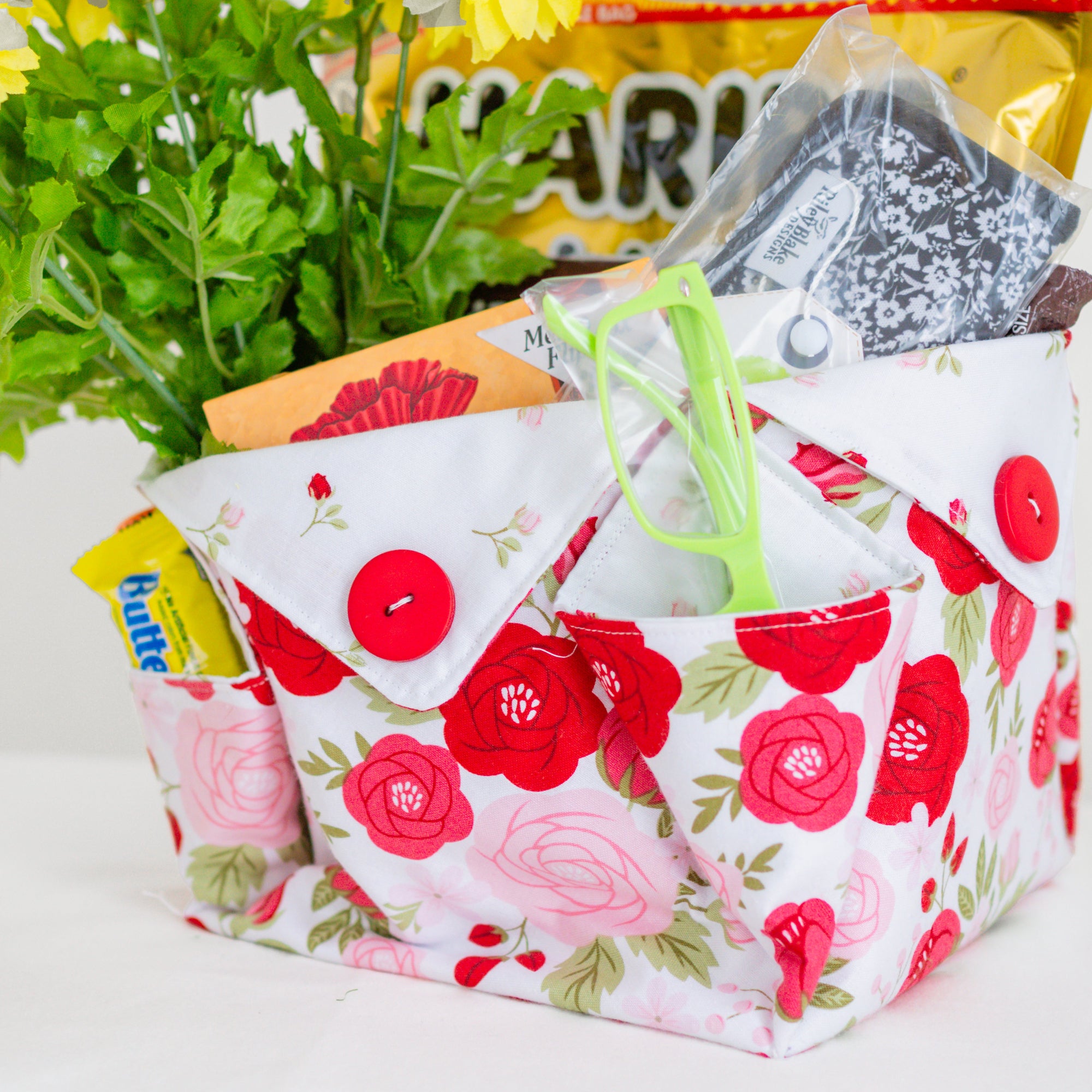 Floral-patterned fabric basket with snacks and a plant on a white surface