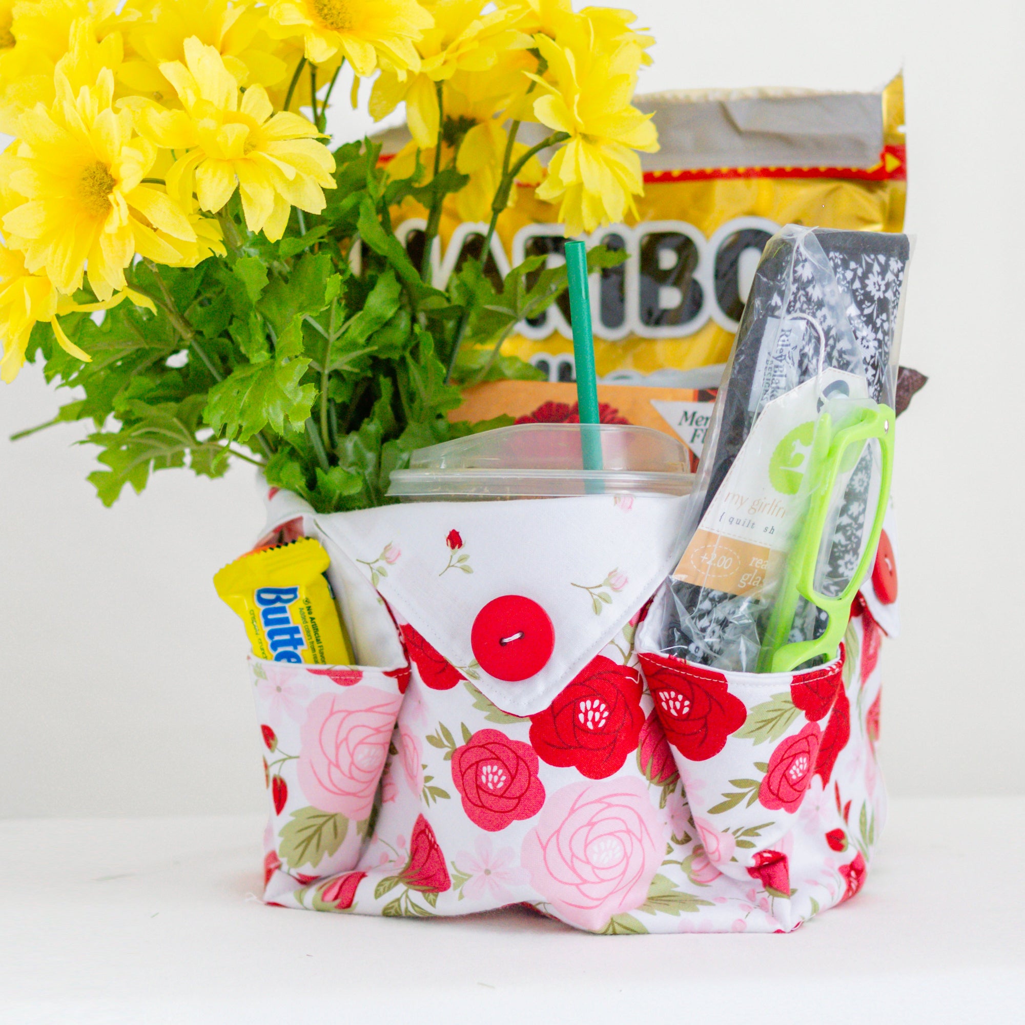 Floral-patterned fabric basket with yellow flowers, magazines, and a butter container on a white background