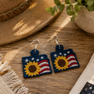 Sunflower-themed earrings on a wooden surface with a hat and plant in the background