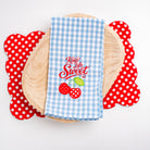 Blue checkered towel with 'Keep Life Sweet' text and cherry design on a wooden plate with red polka dot coasters.
