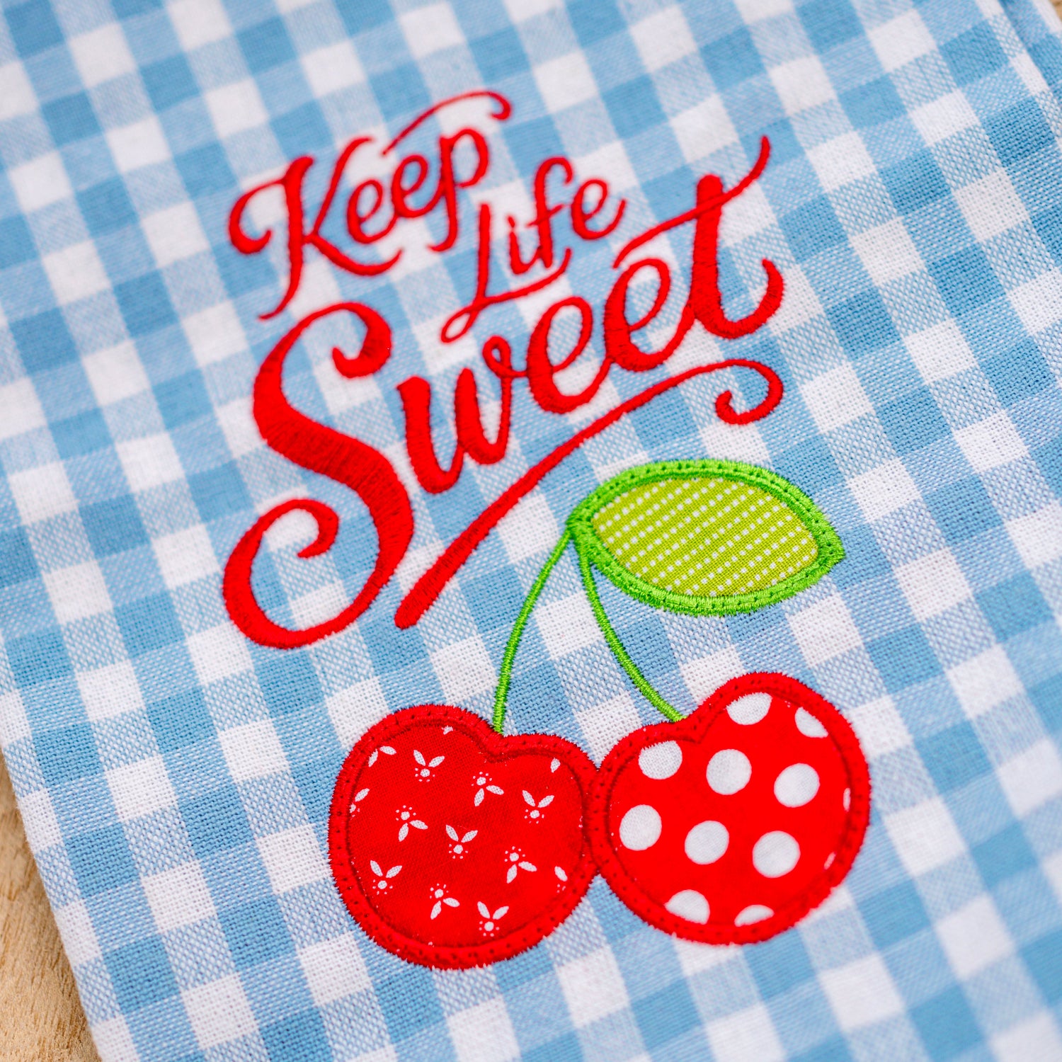 Embroidered towel with 'Keep Life Sweet' text and cherries on a blue checkered background
