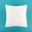 A plain white square throw pillow centered against a solid teal background.