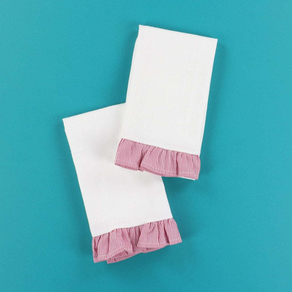 Two white towels with red checkered ruffles on a teal background