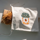 White tote bag with a design of a potted plant and pumpkin on a gray surface.