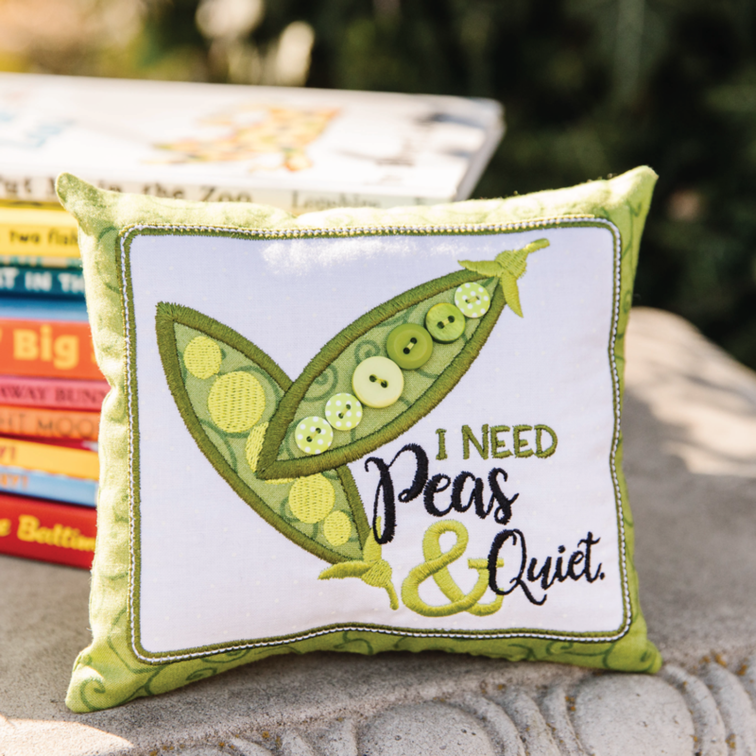 Decorative pillow with a pea design and text 'I Need Peas & Quiet' on a stone surface.