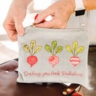Small pouch with embroidered radishes and text held by a person.
