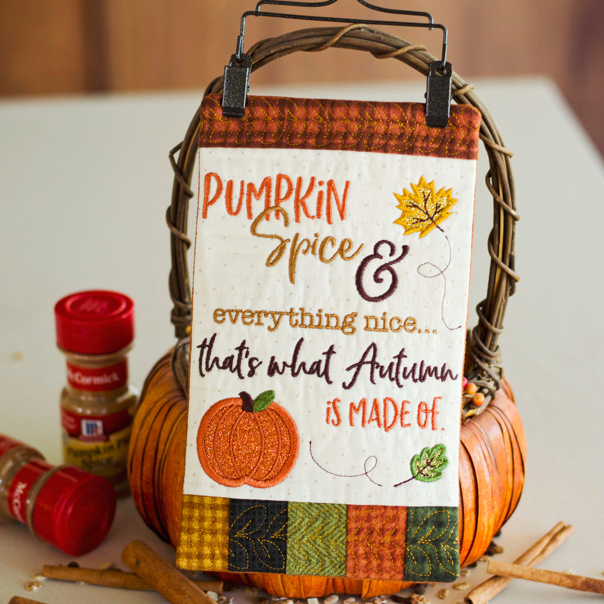 A decorative autumn-themed sign hanging from a wicker basket handle, with the phrase “Pumpkin Spice & everything nice.