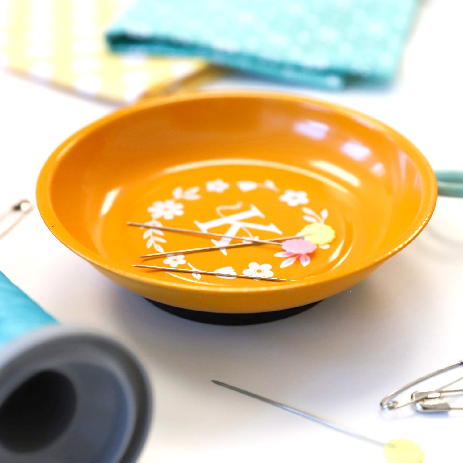 Orange bowl with floral design on a white surface with sewing tools.