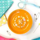 Orange plate with decorative elements on a white surface with sewing supplies.