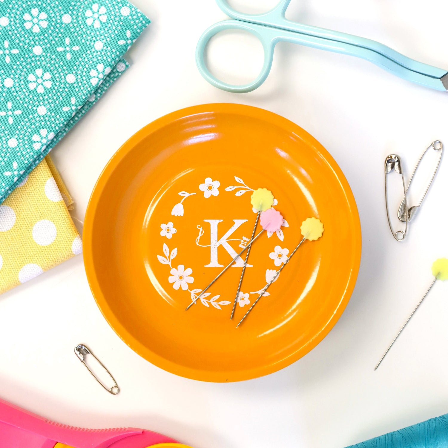 Orange plate with decorative elements on a white surface with sewing supplies.