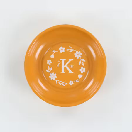 Orange plate with white floral and letter 'K' design on a white background