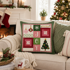 A square Christmas throw pillow with a patchwork quilt design featuring the word 'JOY' and holiday motifs, styled on a beige sofa in a cozy living room with a fireplace, stockings, and a decorated Christmas tree.
