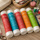 Five Kimberly-Clark Sewing Wax Stabilizers in assorted colors (red, teal, coral, orange, and green) arranged on a wooden table surrounded by sewing and crafting props.