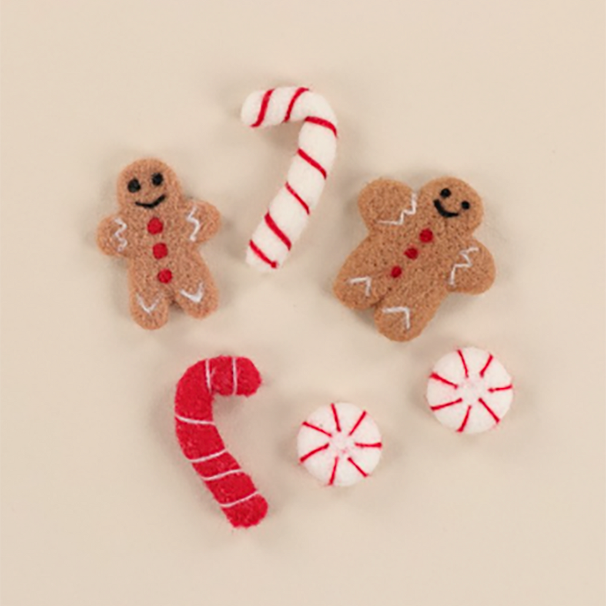 A set of felt Christmas-themed accessories including two gingerbread men, two candy canes, and two peppermint candies, arranged on a solid beige background.