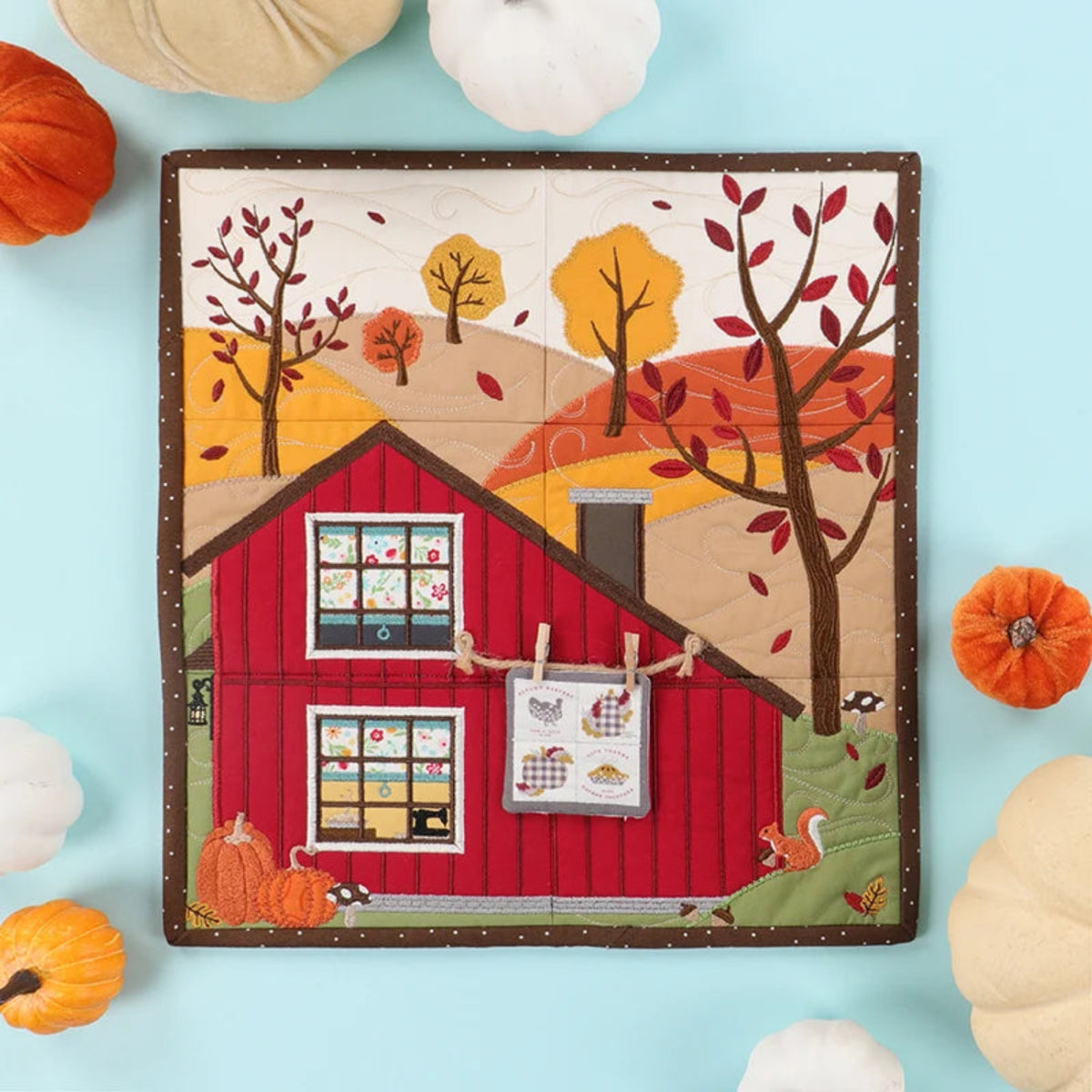 Quilt with a red barn design surrounded by pumpkins on a light blue background