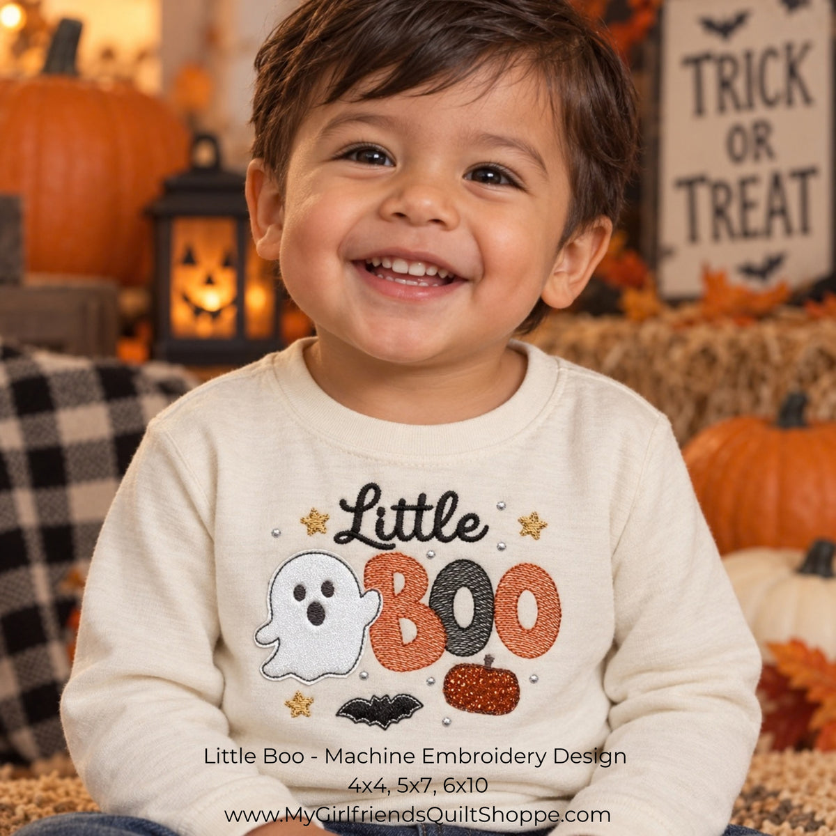A smiling toddler wearing a cream long-sleeve shirt with a 'Little Boo' Halloween machine embroidery design featuring a ghost, orange and black BOO letters, and stars. The background is a cozy, decorated autumn scene with pumpkins, a lantern, and a 'Trick or Treat' sign.