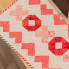 Quilt with red and pink geometric pattern on a wooden surface