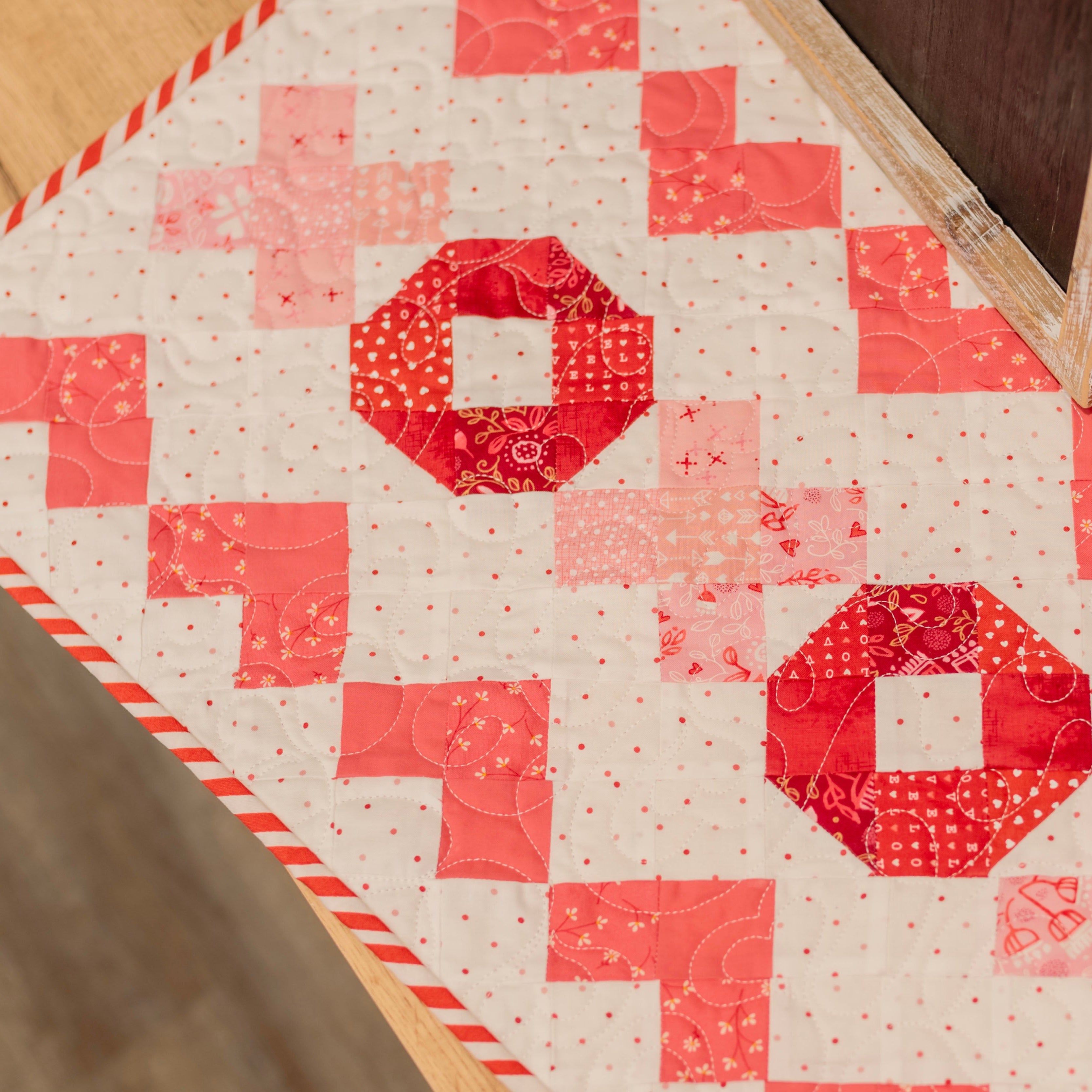 Quilt with red and pink geometric pattern on a wooden surface
