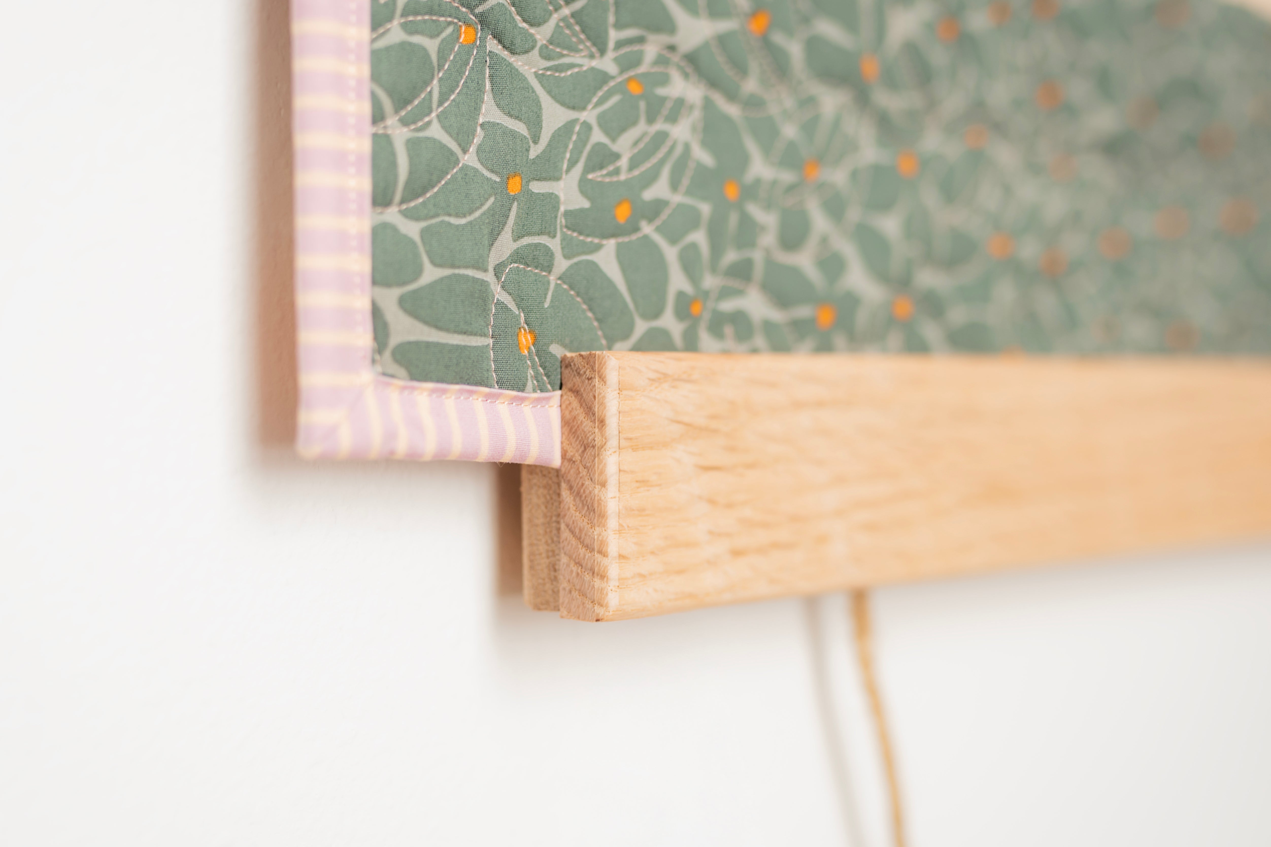 Close-up of a wooden frame with a green patterned paper background on a white wall. 24" wall hanger