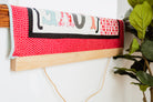 Textile art piece with colorful patterns on a wooden frame against a white wall. 36" wall hanger