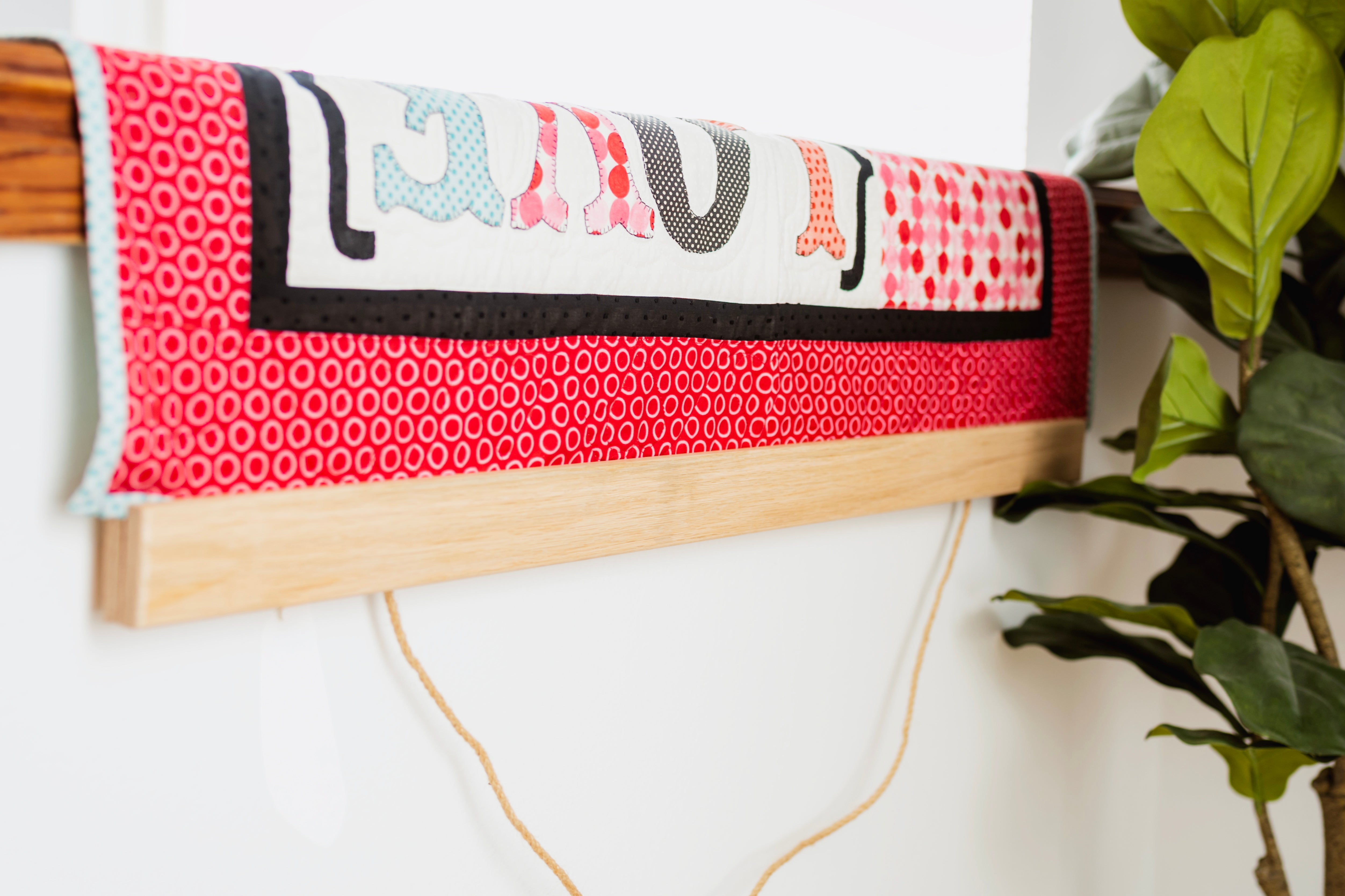 Textile art piece with colorful patterns on a wooden frame against a white wall. 36" wall hanger