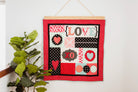 Decorative wall hanging with 'LOVE' and heart designs on a red background, hanging on a white wall. 36" wall hanger