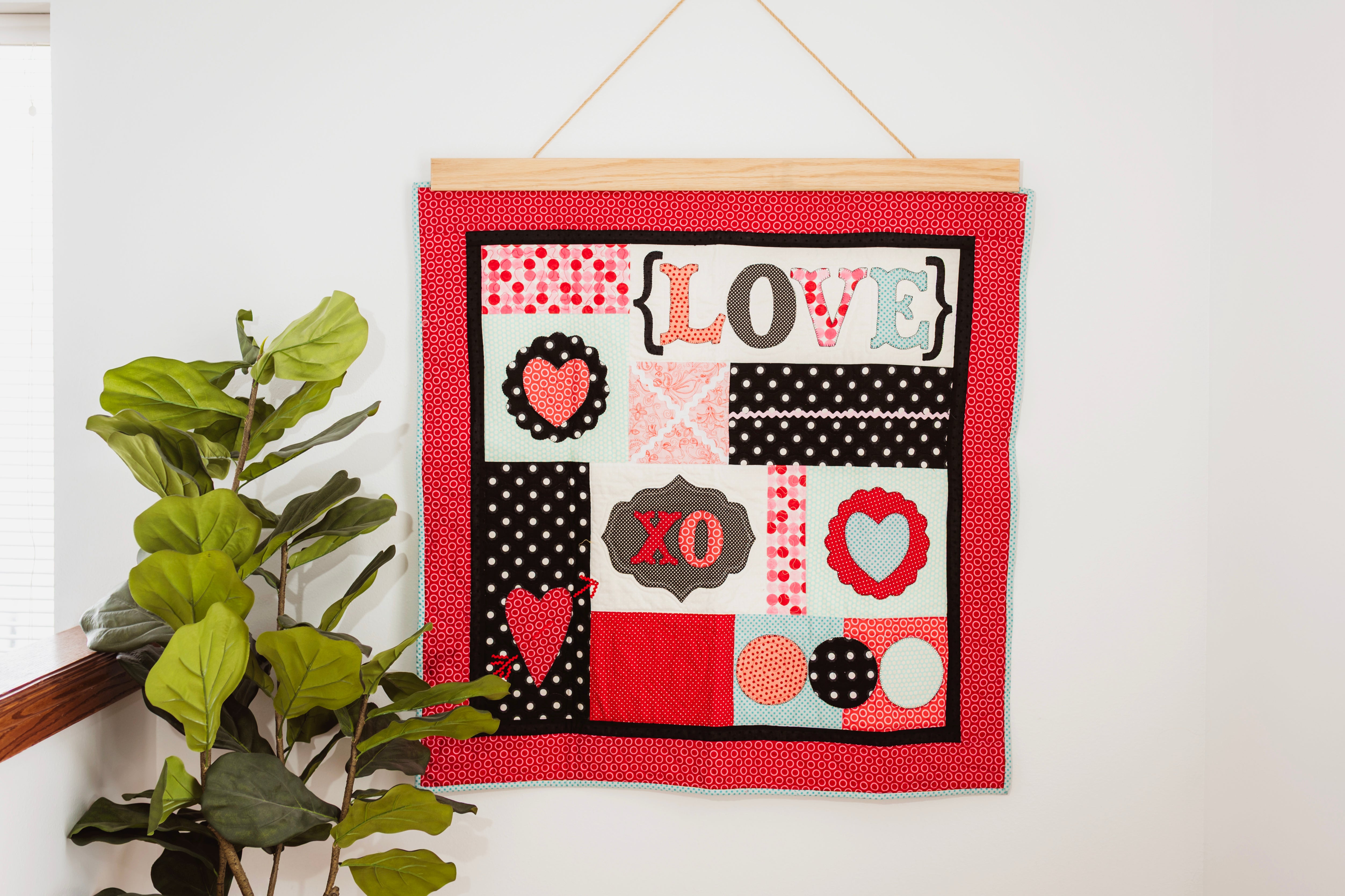 Decorative wall hanging with 'LOVE' and heart designs on a red background, hanging on a white wall. 36" wall hanger