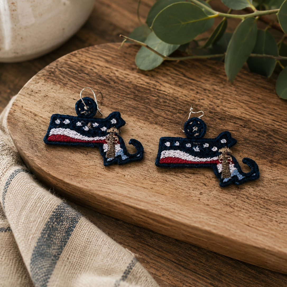 Pair of embroidered earrings on a wooden surface with a plant in the background