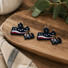 Pair of embroidered earrings on a wooden surface with a plant in the background