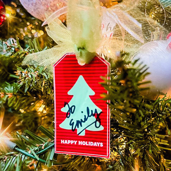 Red tag with a white tree design and 'Happy Holidays' text on a Christmas tree.