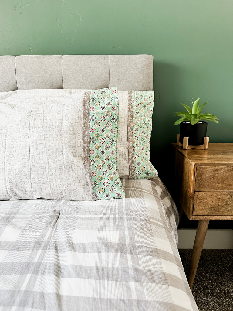 Two white, grey, and mint green pillowcases on a grey bed spread. 