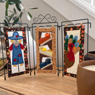 Three small quilted fabric display panels on a black metal stand, styled on a wooden cabinet in a home setting. The left panel features a scarecrow, the center panel shows slices of pumpkin pie and a yellow duck, and the right panel depicts a turkey with a cactus.