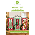 Promotional graphic for a machine embroidery pattern titled 'Mini Quilt Trio: Jingle and Joy' by my girlfriend's quilt shoppe. The design shows three vertical holiday quilt flags hanging on a black metal stand: a green tree on red plaid, a red ornament design on mint green, and a gold 'JOY' lettering on red plaid.