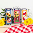 Three decorative panels with sunflower and watermelon designs on a tablecloth with yellow flowers.