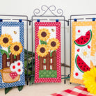 Three decorative panels with sunflowers and watermelon slices on a stand with flowers around.