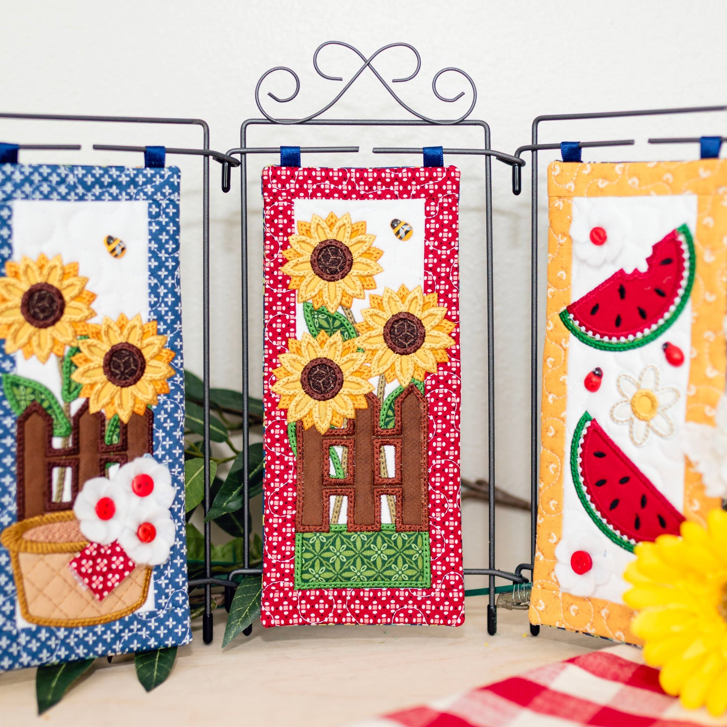 Three decorative panels with sunflowers and watermelon slices on a stand with flowers around.