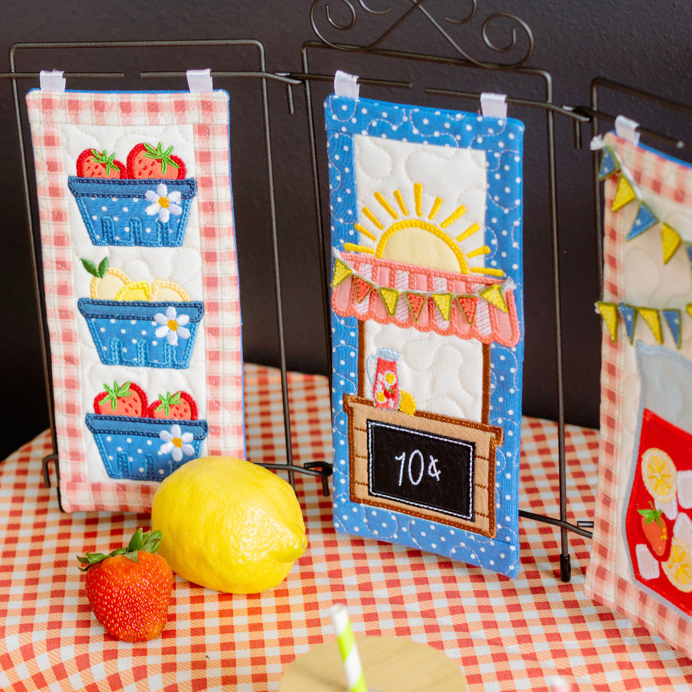 Decorative kitchen towels with summer-themed designs on a checkered tablecloth.