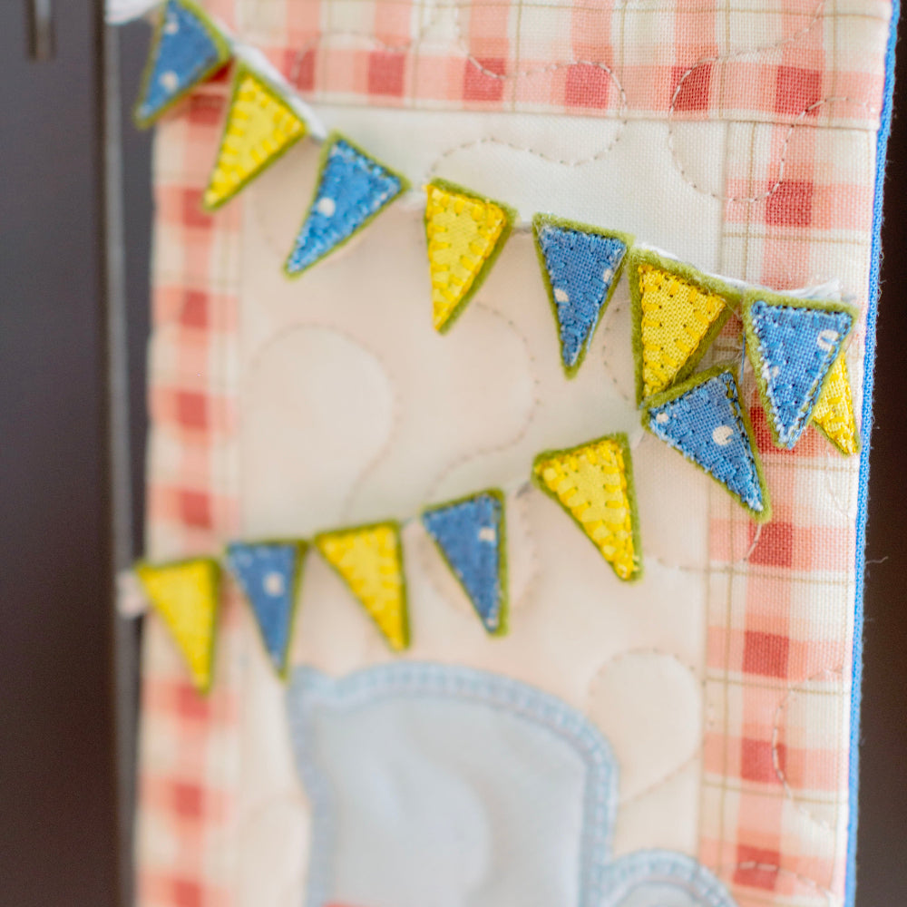 Decorative kitchen towel with a teacup design and colorful bunting on a checkered background