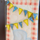 Decorative kitchen towel with a teacup design and colorful bunting on a checkered background