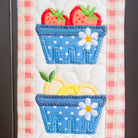 Embroidered design of blue baskets with strawberries and lemons on a checkered fabric background