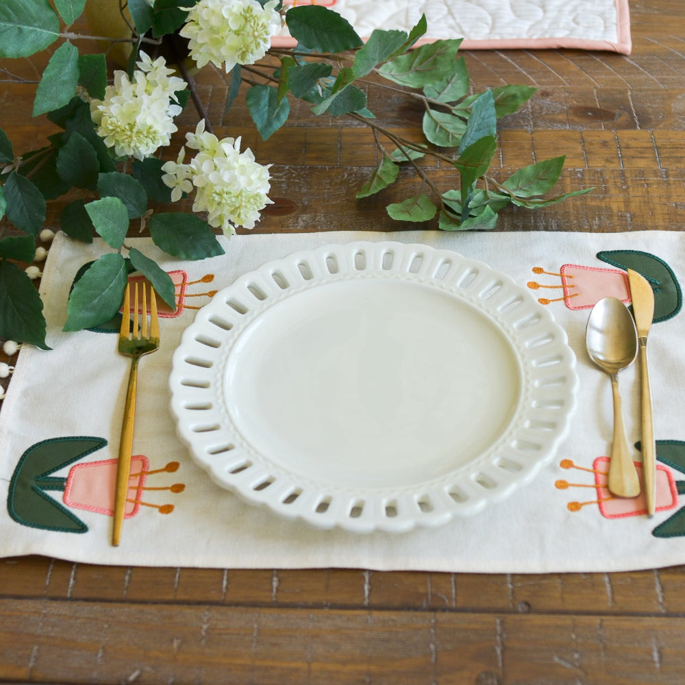 Set table with white plate, gold fork, and spoon on a decorative placemat with floral design.