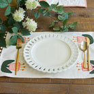 Set table with white plate, gold fork, and spoon on a decorative placemat with floral design.