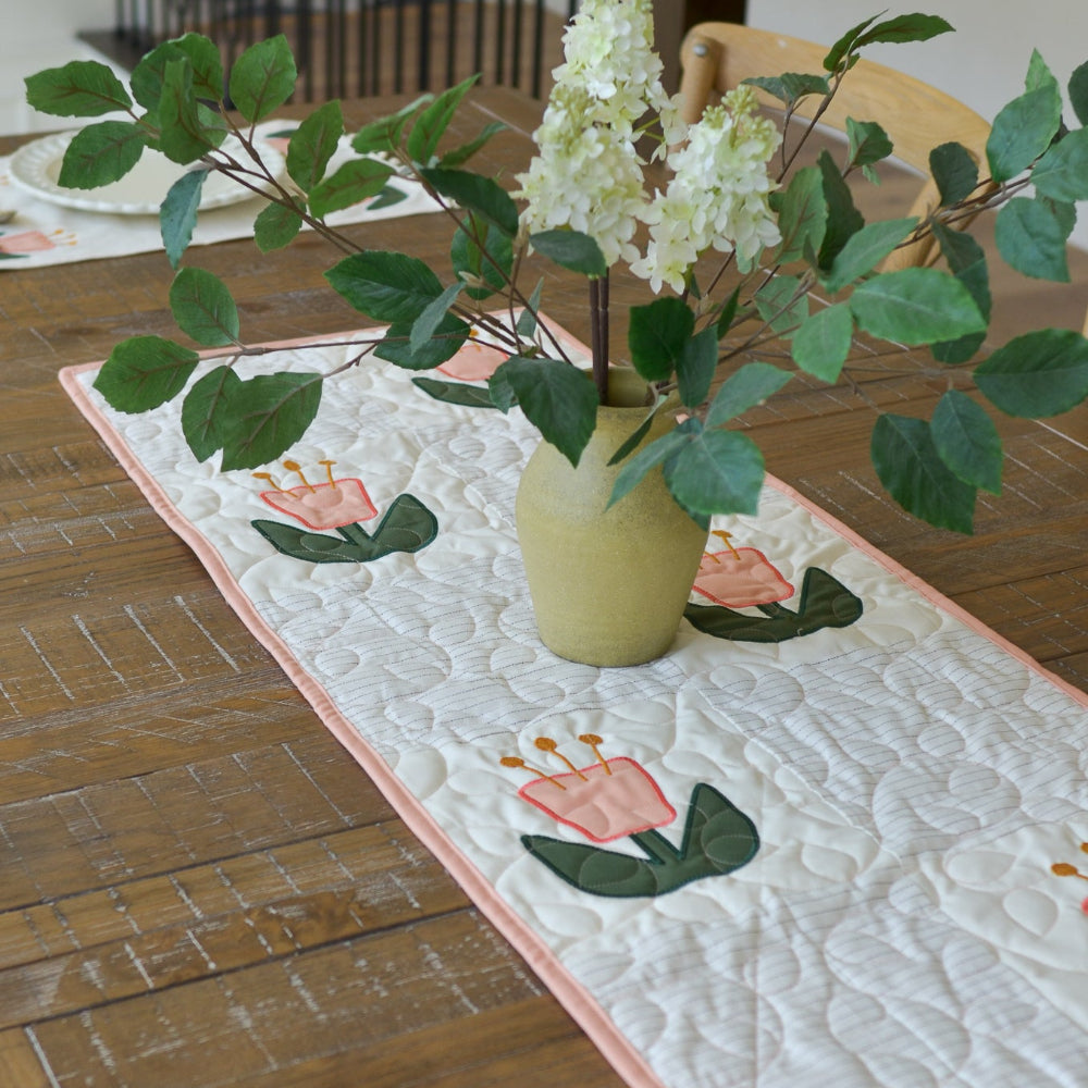 Table setting with a floral table runner and vase on a wooden table.