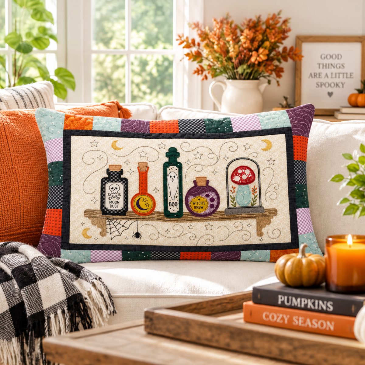 A square decorative throw pillow with a Halloween-themed patchwork border and central illustration of potion bottles, a spiderweb, and a mushroom, styled on a white sofa in a cozy autumn living room setting.