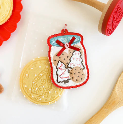Decorative cookie with a jar design on a white surface with cookies and a wooden spoon.