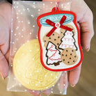 Hand holding a decorative ornament with Christmas cookies and trees on a clear polka dot bag.