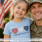 Man in military uniform with a young girl wearing a t-shirt with heart designs and text, American flag in the background.
