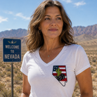 Woman wearing a white t-shirt with a Nevada state design in a desert landscape with a 'Welcome to Nevada' sign.